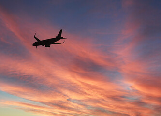 Silhouette of a passenger jet approaching an airport to land against a dramatic sunset sky. Copy...