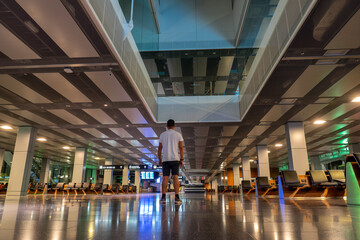 man with his back turned inside the Zurich airport atrium on a night with no passenger movement. ...