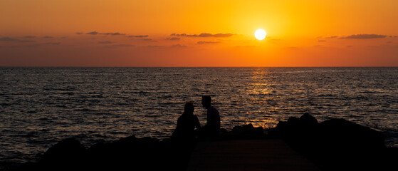 romantic image of an unrecognizable couple at sunset on the beach on top of rocks, image taken in...
