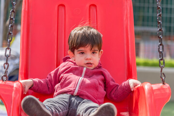 Little boy swinging at the playground in the park.