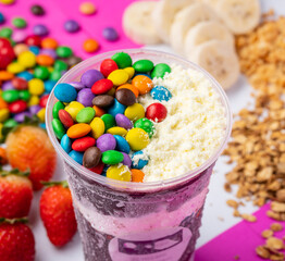 close up of acai or açaí smoothie cup with topping confetti and powdered milk in colorful...