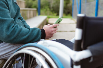 man in wheelchair using mobile phone outdoors