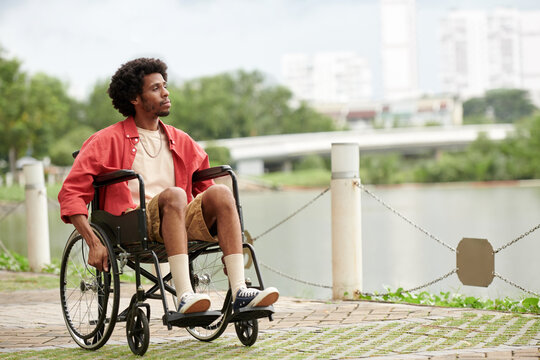 Young Black man sitting in wheelchair outdoor looking at big city in background