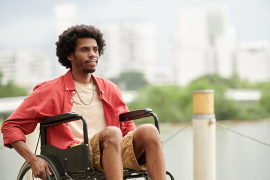 Portrait of smiling pensive Black man sitting in wheelchair and looking away - Powered by Adobe