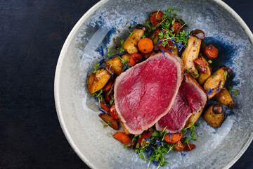 Fried Italian chianina beef fillet steak very rare with mushrooms and carrots served as top view in a Nordic design bowl with copy space left