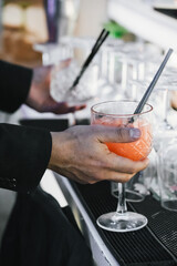 Unrecognizable bartender dressed in black serving a bitter orange cocktail