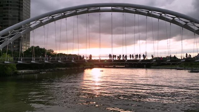 People walking on a bridge with sunset behind them.  Pedestrian bridge on a cloudy evening at Humber Bay
