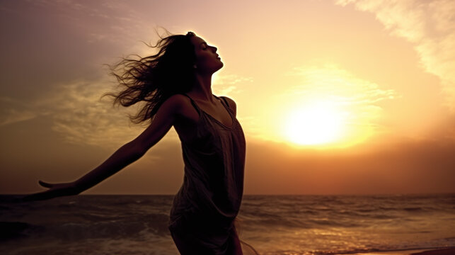 Black silhouettes in front of an orange sunset of a woman who, in a relaxed pose, puts her arms in the air and lifts her head into the last rays of sunshine of the day