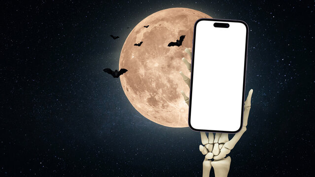 Skeleton hand holds a mock up smartphone with the full moon and bats, a creative idea. App and phone, concept. Halloween advertising. Copy space for design and text