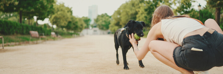 Girl walks along the path in the park with back dog.