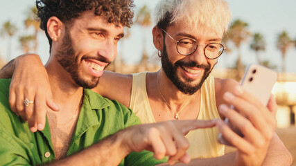 Close-up of young gay couple sitting embracing, smiling and laughing have fun with mobile phone...