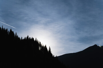 Night in the Tatra mountains, the moon rises above the silhouettes of trees near the rocks.