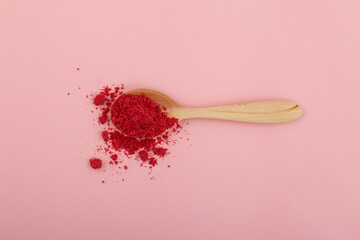 Dried raspberries powder in wooden spoon on pink background. Dehydrated fruits in powder are often added to drinks, cocktails, smoothies and porridges for breakfast - obrazy, fototapety, plakaty