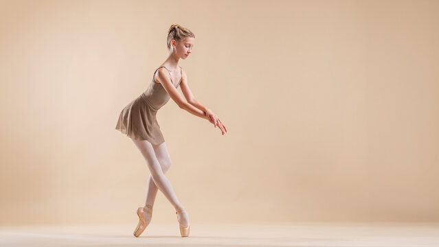 Fototapeta Beautiful young girl professional student ballerina in pointe shoes and a leotard on a light beige background.