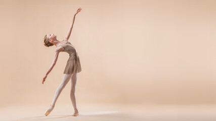 Beautiful young girl professional student ballerina in pointe shoes and a leotard on a light beige background.