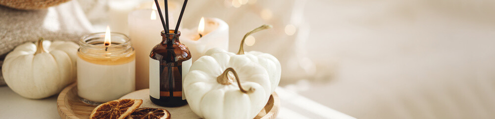 Autumn cozy mood composition on the windowsill. Aroma diffuser, pumpkins, dry citrus, candles on wooden tray, knitted warm plaid. Fall hygge home decor, aromatherapy. Copy space, banner white 