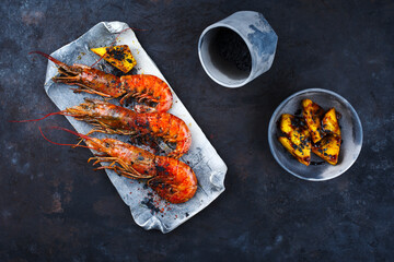 Traditional fried king prawns with pineapple pieces and black salt served as top view on a design tray with text space