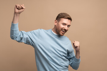 Happy man rejoices raising fists up. Middle aged guy smiles cheerfully happily brightly...