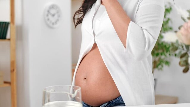 Pregnant woman with belly pouring pure water from jug to glass healthy lifestyle wellness closeup