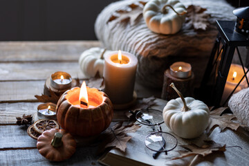 Fototapeta na wymiar Atmospheric candle - shape of pumpkins, autumn decor, book on grey fall rainy day. Autumn cozy home atmosphere, inspiration, hygge concept. Aromatherapy, warming, relaxation. Wooden background