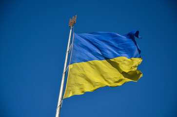 National flag of Ukraine on flagpole with trident waving in the wind with blue clear sky on background. Freedom and patriotism concept