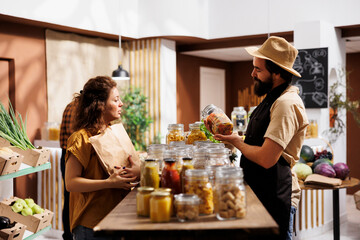 Customer shopping for vegan ecofriendly pantry staples in zero waste supermarket, being assisted with information by merchant. Vendor showing woman homegrown pasta perfect for healthy eating