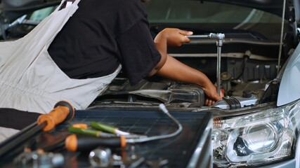 Trained technician in garage using torque wrench to tighten bolts inside opened up vehicle, preparing to change oil. Auto repair shop professional doing checkup on car to prevent issues, close up shot