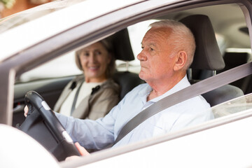 Elderly man and woman driving a car in the city. Man driving a car