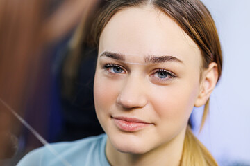 The master marks the woman's face before permanent eyebrow makeup. Eyebrow tattoo. Beauty procedure...