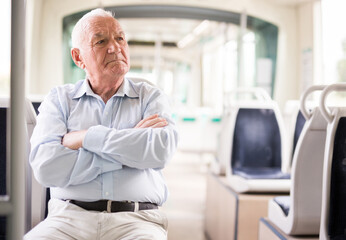 Fototapeta premium Senior European man sitting on seat inside tram and waiting for his stop.