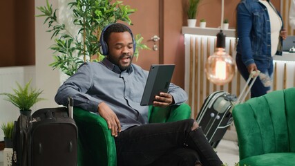 Man waving at videocall connection in hotel lounge area, calling family to ensure travelling safety...