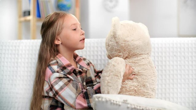 Casual blonde female kid hugging talking to bear toy secret gossiping trust support home white room