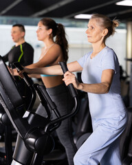 Fototapeta premium Elterly fitness woman in sportswear doing cardio training on ellipsoid in gym