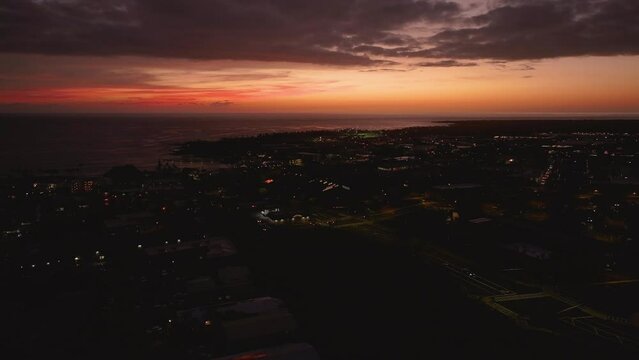 Aerial Kona Hawaii city dark red sunset cityscape. Big Island. Luxury exclusive resorts homes on coast with tropical landscape. Economy is tourism based. Water and tropical beach recreation and fun.