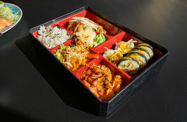Japanese Lunch in Bento Box with Deep-Fried Squid Rings, Sushi Rolls, Salad, Rice, Pickled Ginger