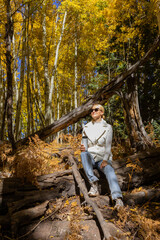 Obraz premium Pretty Woman Sits On Fallen Tree And Drinks Hot Beverage From Thermos Travel Mug In Forest, Nature, Wears Warm Clothes. Autumn Drink, Fall Leaves Season. Zero Waste. Vertical. Copy Space.