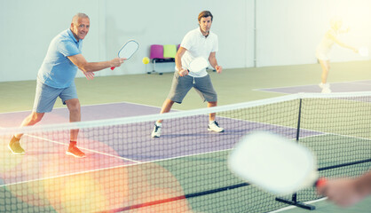 Two athletic men of different ages are playing a game of pickleball on a court inside a sports...