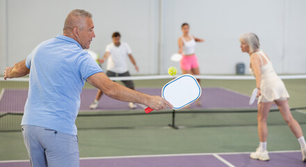 Rear view of senior man with white racket playing pickleball tennis at court