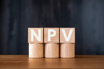 There is wood cube with the word NPV. It is an abbreviation for Net Present Value as eye-catching...