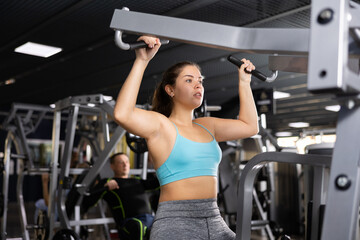 Fototapeta na wymiar Young woman trains her arm muscles using a simulator in the gym