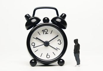 Selective focus of miniature staring at alarm clock on white background.