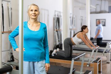 Fototapeta na wymiar Portrait of mature female in sportswear smiling at camera while standing in Pilates rehabilitation center