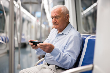 Old European man sitting inside subway train and using his smartphone while waiting for next stop.