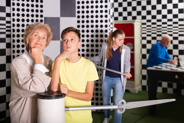 Grandmother and grandson standing in escape room and thinking about solution of conundrum. Teenager girl with big metal clock hand going to them to say something.