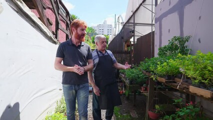 Senior Gardener Assisting Customer at Plant Store. Horticulturist culture in Flower Shop backyard of senior person showing plants to young man