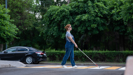 Blind pregnant woman crosses the road at a crosswalk with a cane. 