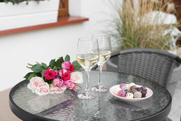 Bouquet of roses, glasses with wine and candies on glass table on outdoor terrace