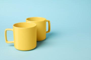 Two yellow ceramic mugs on light blue background, space for text
