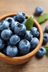 Bowl of tasty fresh blueberries with green leaves on wooden table, closeup