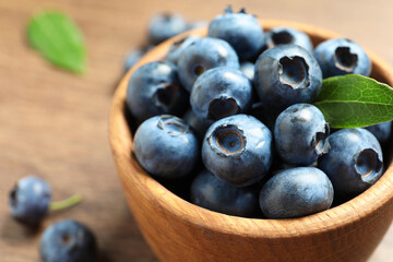 Bowl of tasty fresh blueberries with green leaves on table, closeup. Space for text